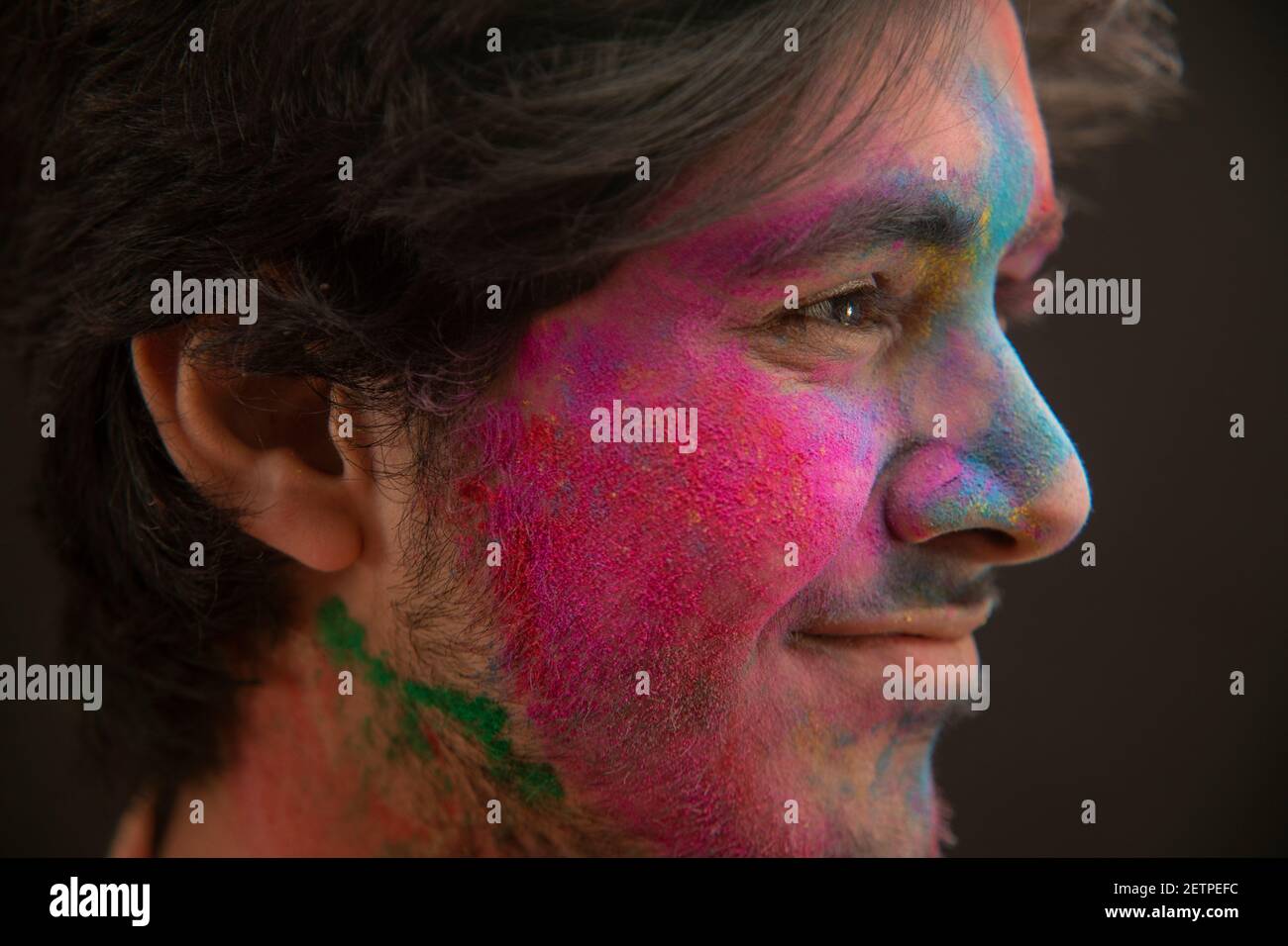 SIDE SHOT OF A HAPPY MAN WITH HOLI COLOURS ON HIS FACE Stock Photo