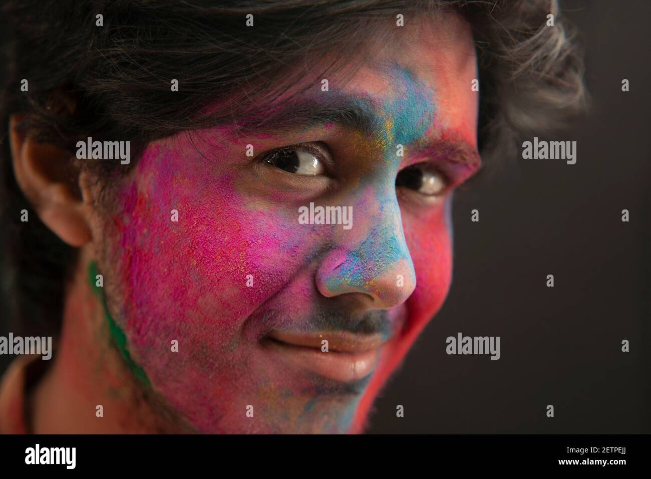 A YOUNG MAN WITH GULAL ON HIS FACE PLAYFULLY LOOKING AT CAMERA Stock Photo