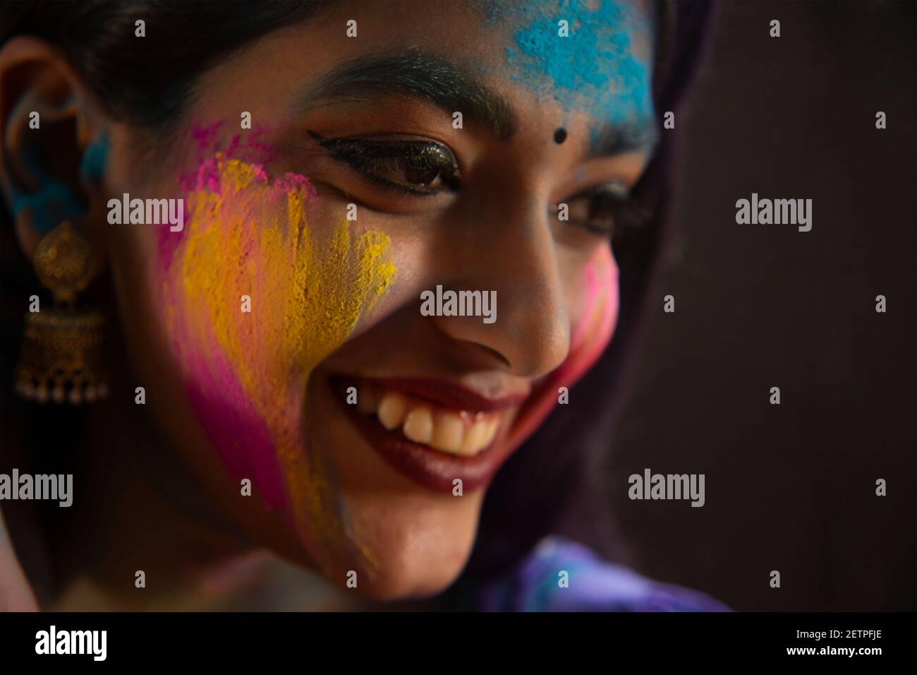 SIDE SHOT OF A HAPPY YOUNG WOMAN WITH GULAL ON HER FACE Stock Photo