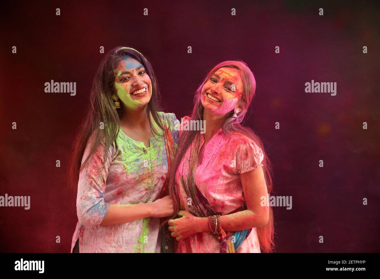TWO YOUNG WOMEN HAPPILY POSING TOGETHER WHILE CELEBRATING HOLI Stock Photo