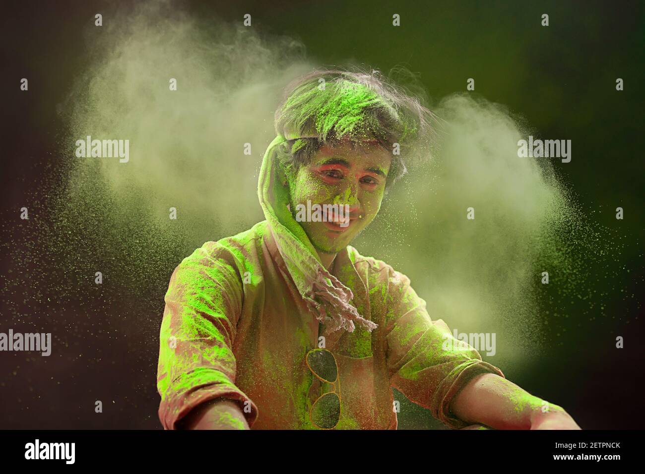 A YOUNG MAN SITTING AROUND HOLI COLOURS LOOKING AT CAMERA AND SMILING Stock Photo