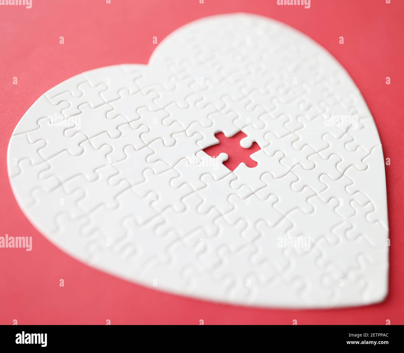White heart made from puzzle lying on red background Stock Photo