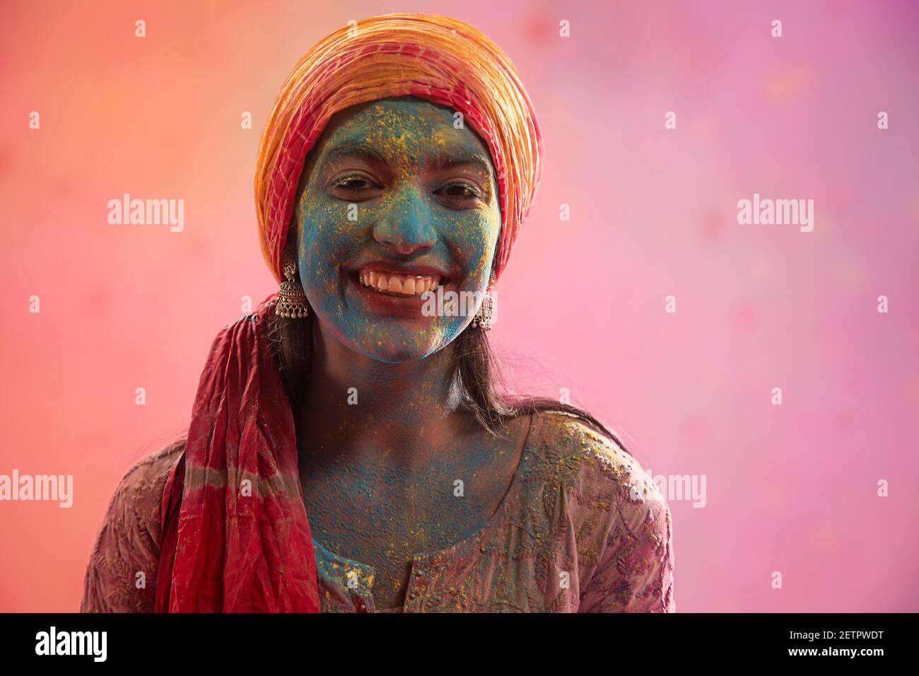 PORTRAIT OF HAPPY YOUNG WOMAN WITH DUPATTA TIED AS PAGDI ON HEAD AND HOLI COLOUR ALL OVER Stock
