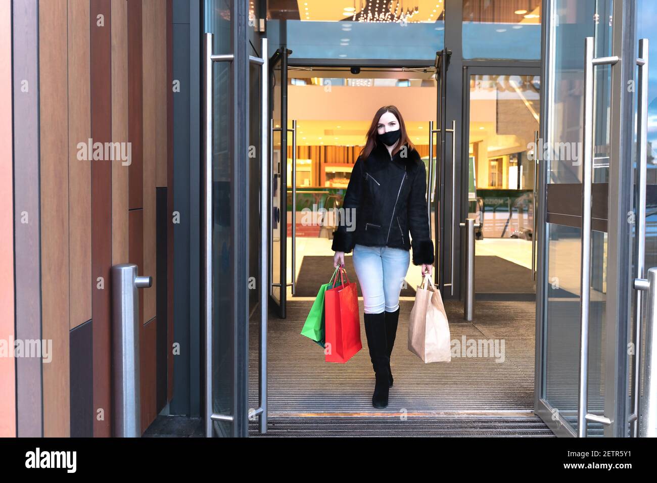 Beautiful woman in protective mask with shopping bags walks out mall. Stylish shopper girl Stock Photo