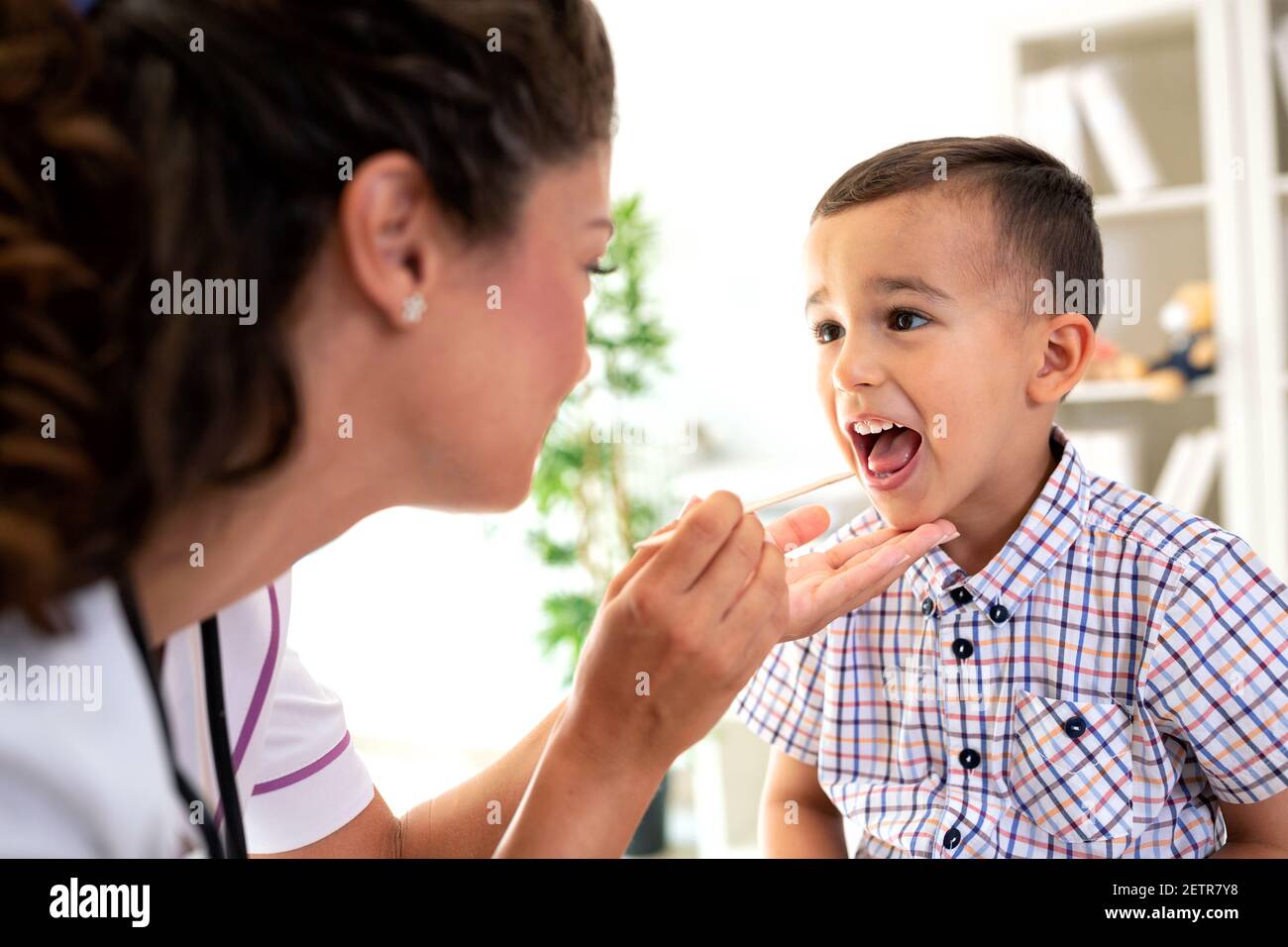 Well trained physician checking the throat of a kid using a wooden