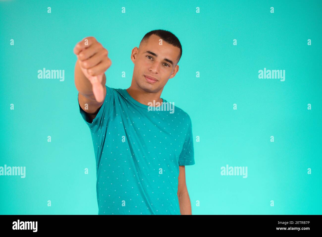 Cool young latin man with thumb down over green background. Stock Photo