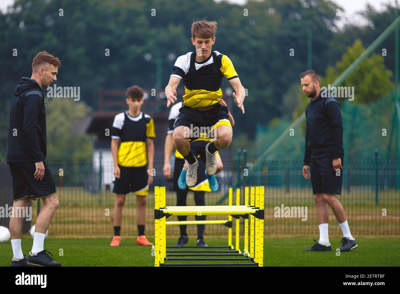 Youth Soccer Team on Training. Young Boys in Football Club Practicing Durability. Teenage Boy Jumping High Over Hurdle Obstacles. Young Men Coaching S Stock Photo