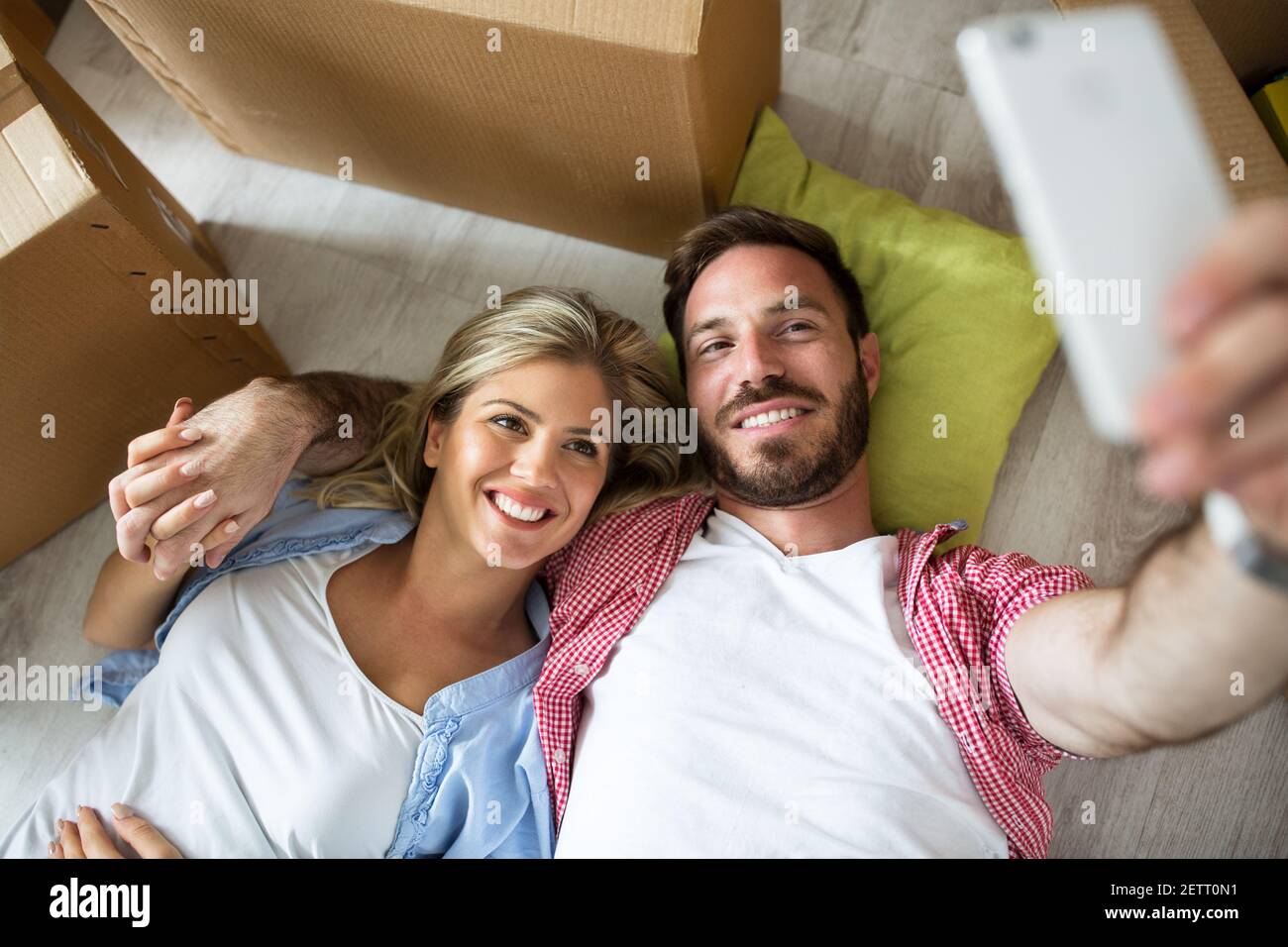 Young couple taking a selfie and celebrating moving to new home sitting ...