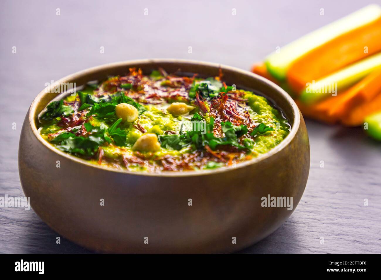 Homemade chickpea green hummus with herbs in round bamboo bowl, celery