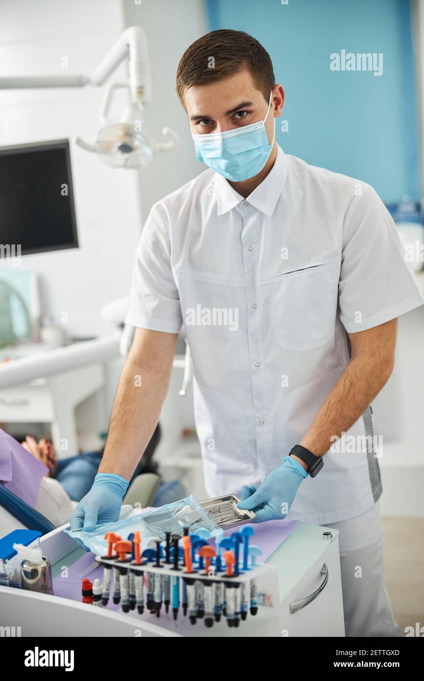 Man in white scrubs getting dental tools from plastic bag Stock Photo