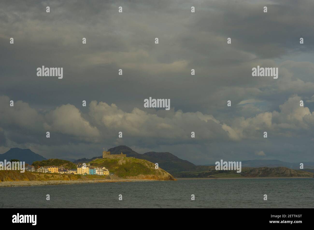 Criccieth lit by sunlight for the beach at Llanystumdwy with the hills of Snowdonia under storm clouds. Stock Photo