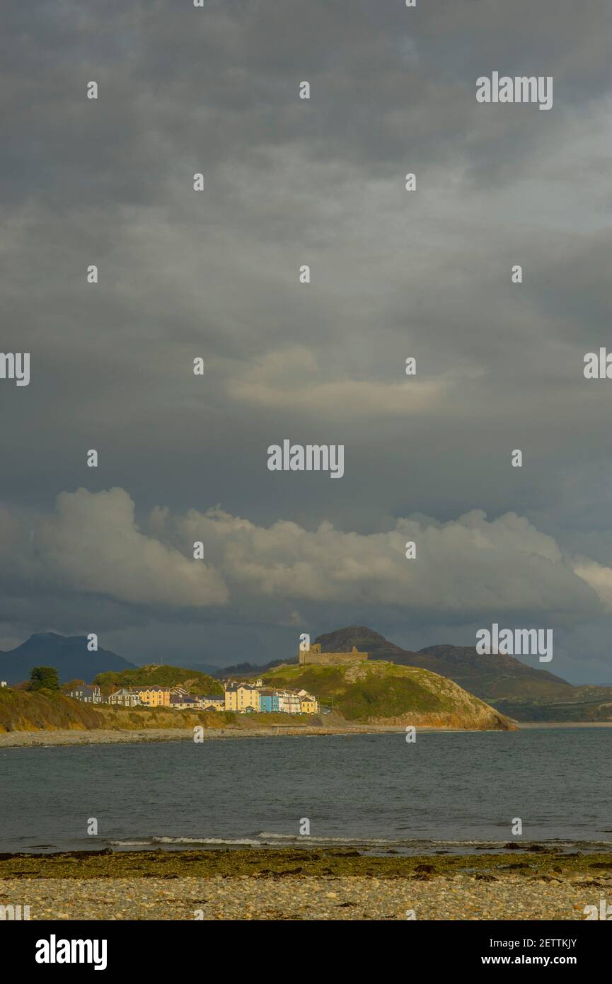 Criccieth lit by sunlight for the beach at Llanystumdwy with the hills of Snowdonia under storm clouds. Stock Photo