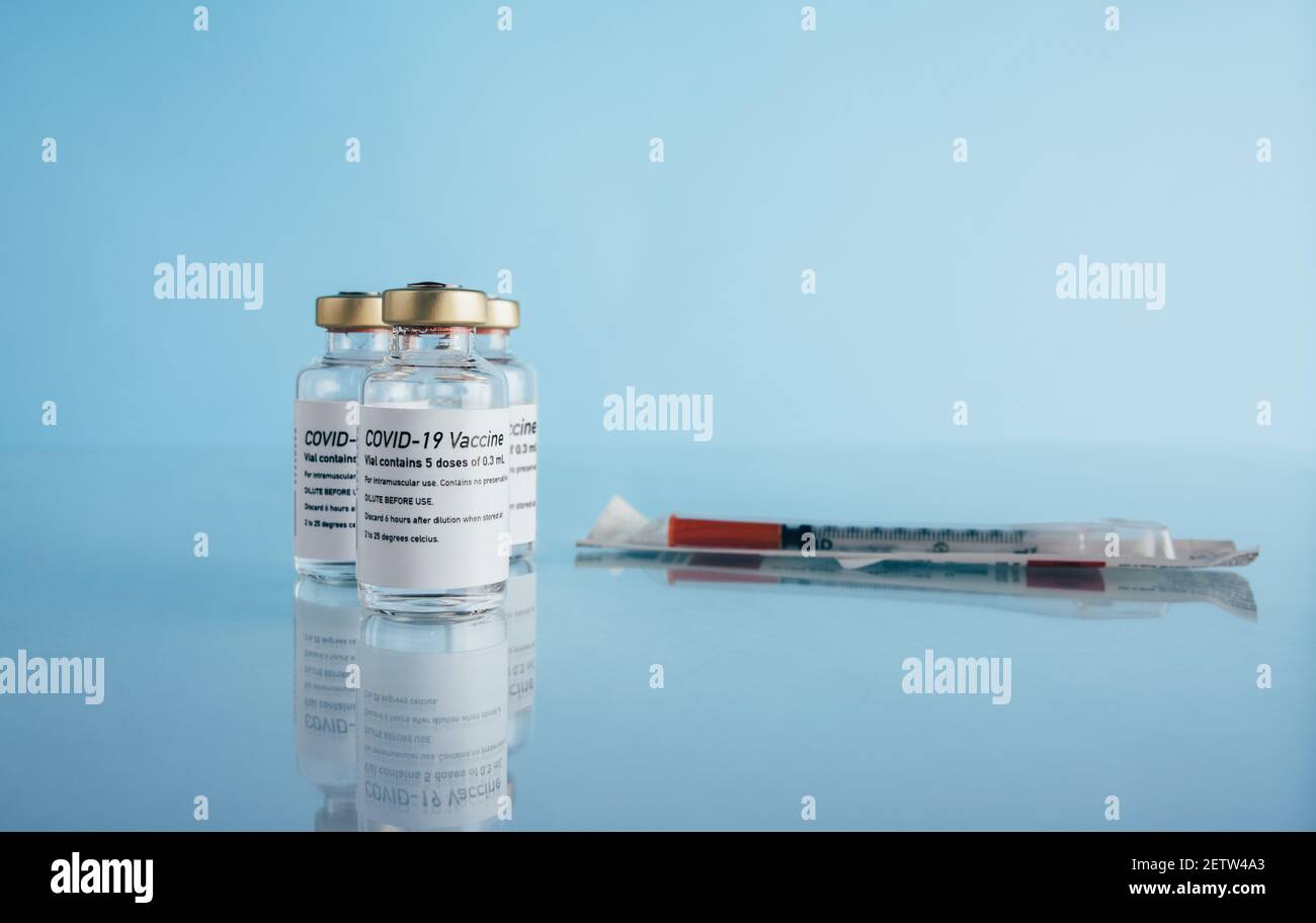 Corona virus immunity vaccine vials and syringe on blue background. Covid-19 vaccination bottles with injection on reflective surface. Stock Photo