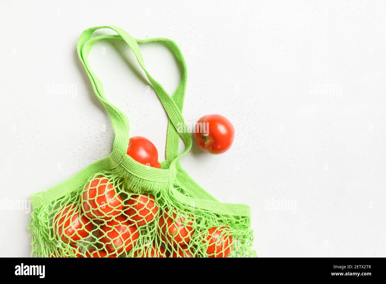 Shopping green mesh bag with tomatoes on white table. Zero waste. Healthy goods. View from above. Grow food. Copy space. Stock Photo