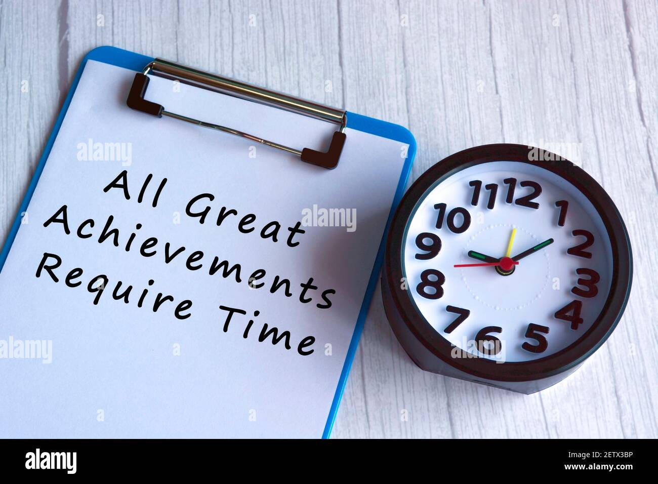 Motivational quote on blue clip board with alarm clock on wooden desk