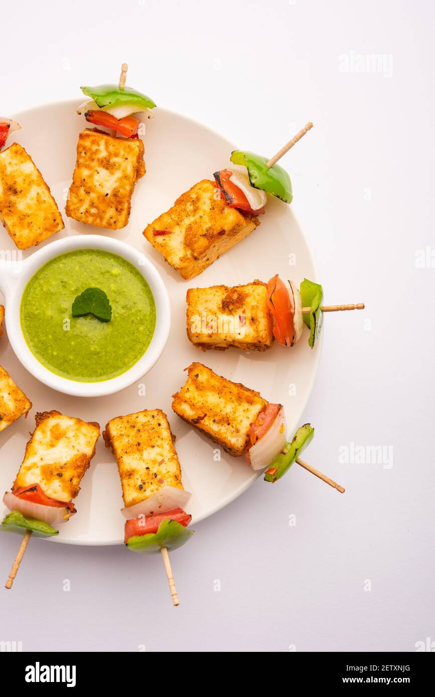 Starter snack Paneer Tikka with stick in plate with green chutney