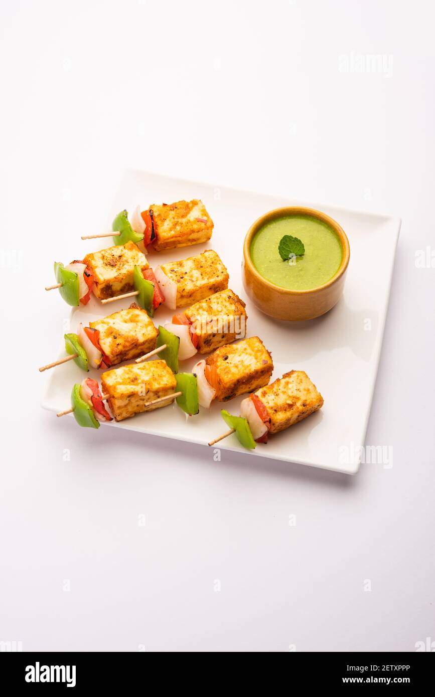 Starter snack Paneer Tikka with stick in plate with green chutney