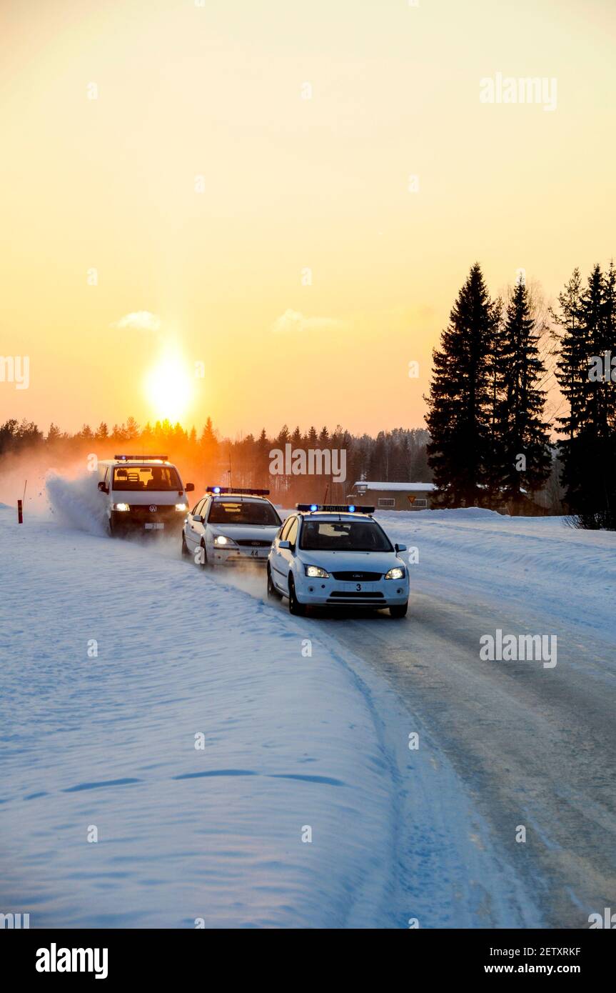 A convoy of blue flashing Finnish Traffic Police car speeds along a snow-covered road as the winter sunsets at Pieksamaki in Finland.  The Police were Stock Photo