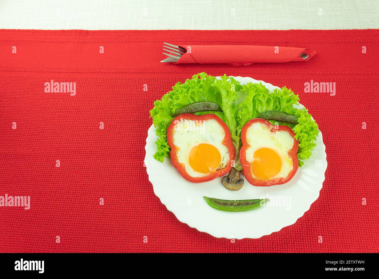 Scrambled eggs, fried eggs, with vegetables in the form of a cheerful face. Two fried eggs with paprika and green peas in the form of a smiley Stock Photo