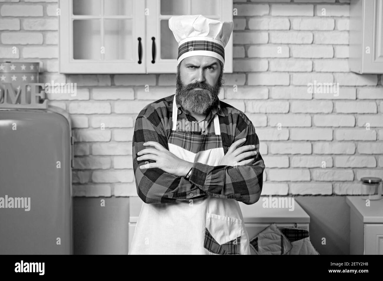 Handsome bearded cook chef in white uniform and hat with long lush moustache on serious face standing and hands clasped. Stock Photo