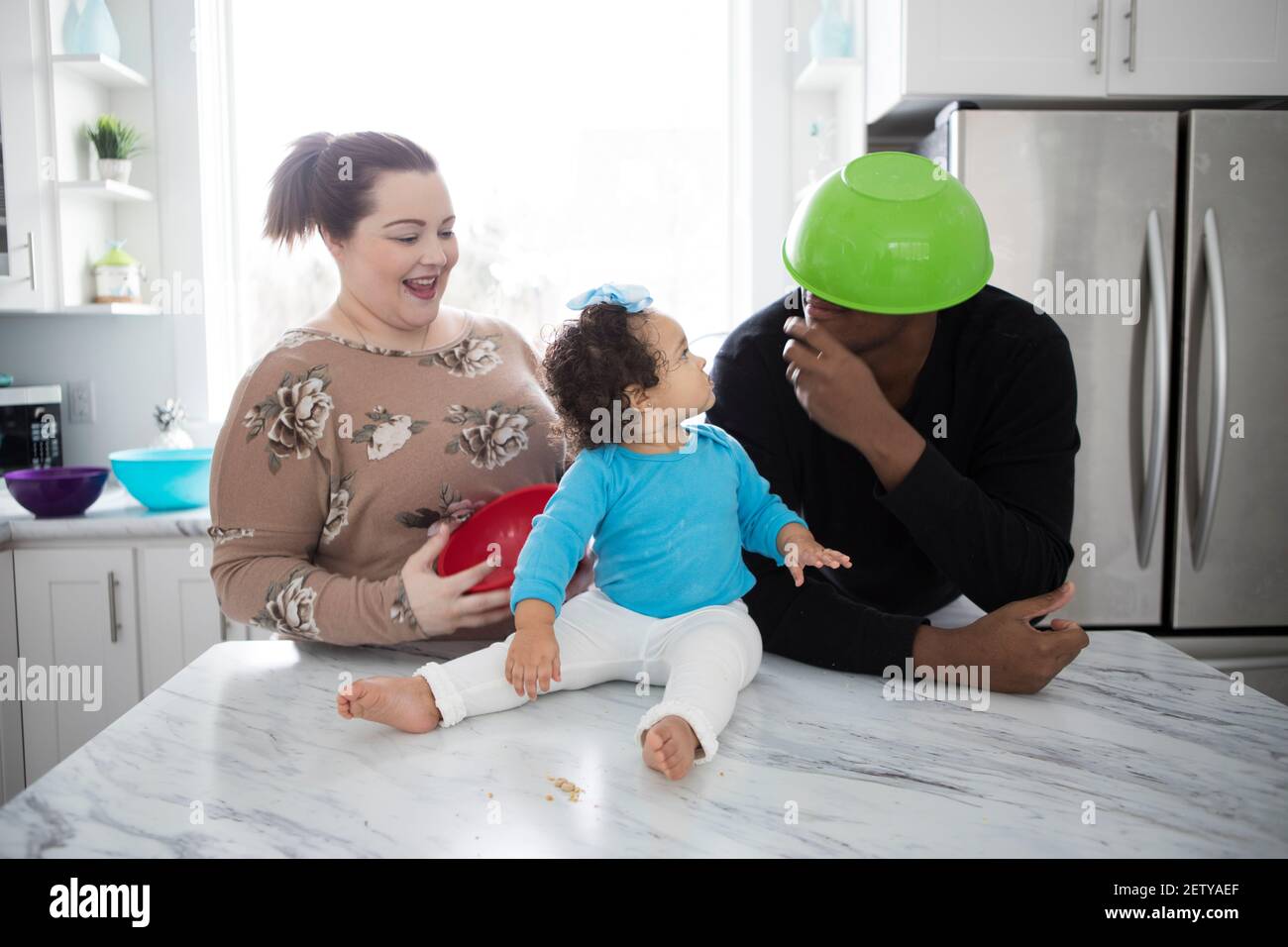 A happy interracial couple in a modern kitchen with their little girl. Stock Photo