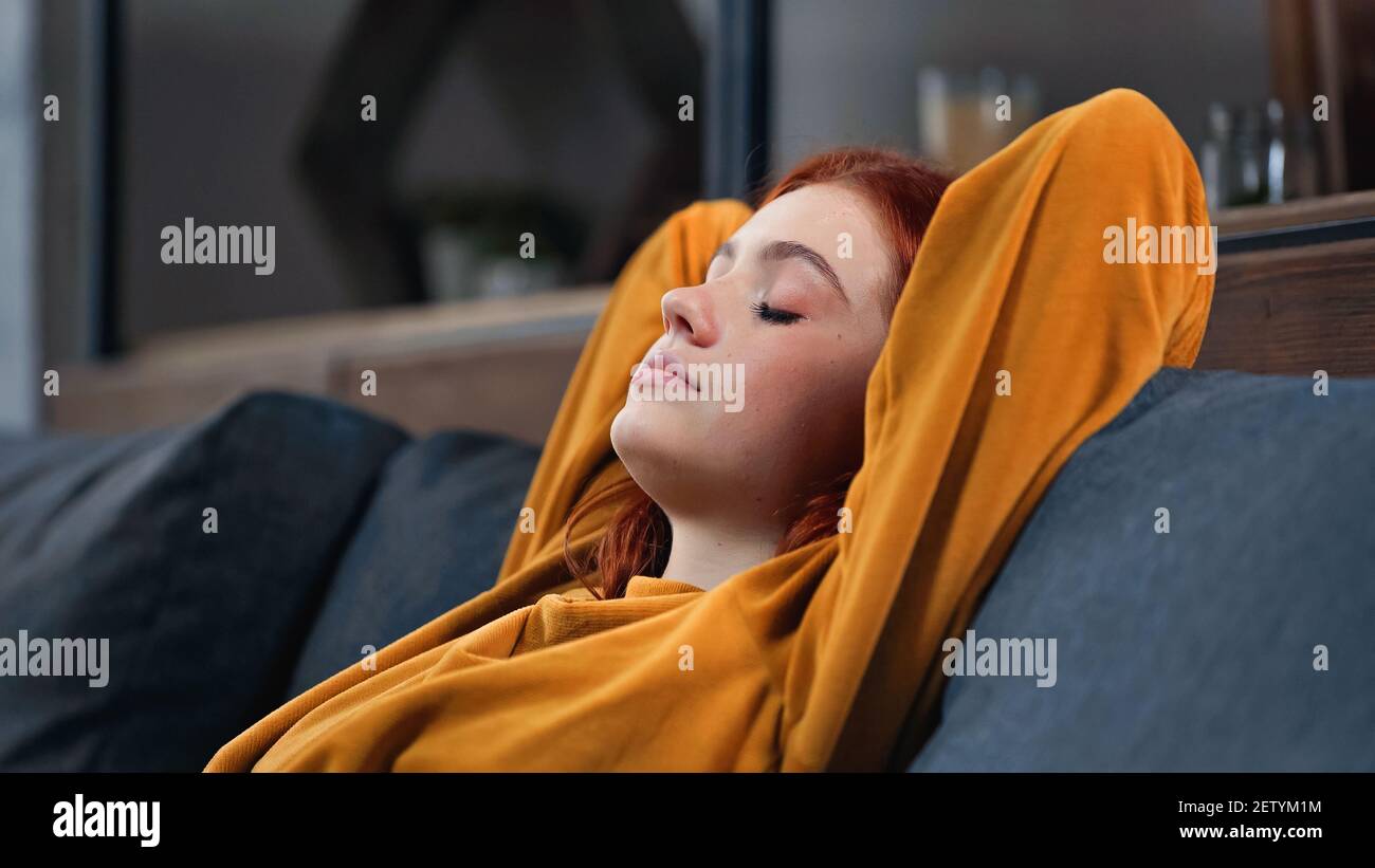 Red haired girl sitting with closed eyes on couch Stock Photo - Alamy