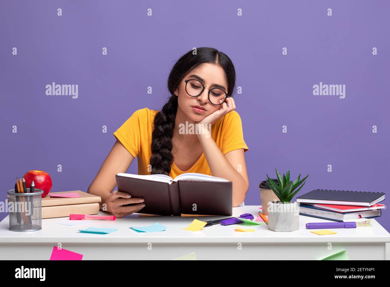 Tired indian woman sitting at desk and reading book Stock Photo - Alamy