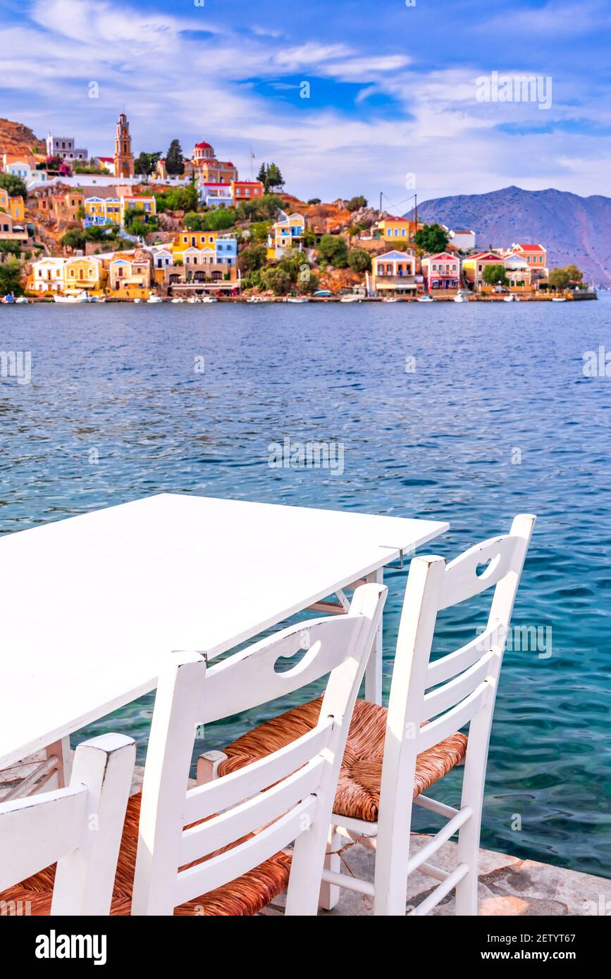 Symi, Greece. Typical Greek tavern white chairs with tables, sea in Rhodes. Stock Photo