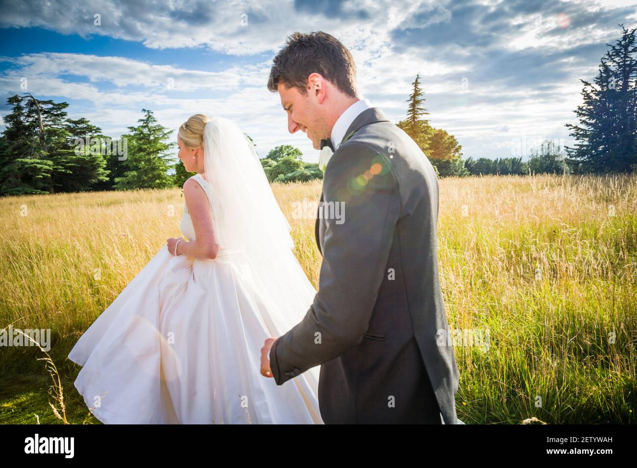 Bride and Bridegroom newly-weds walking through the long grass of the mansion grounds just after they got married.The bride is leads the walk. Stock Photo