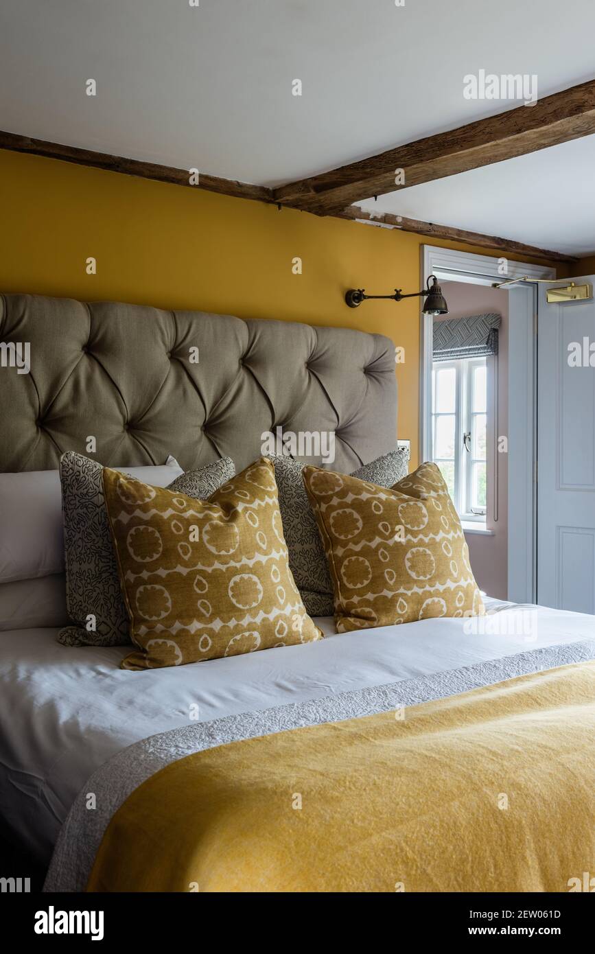 Buttoned headboard and yellow accent in off-grid farmhouse renovation. Stock Photo