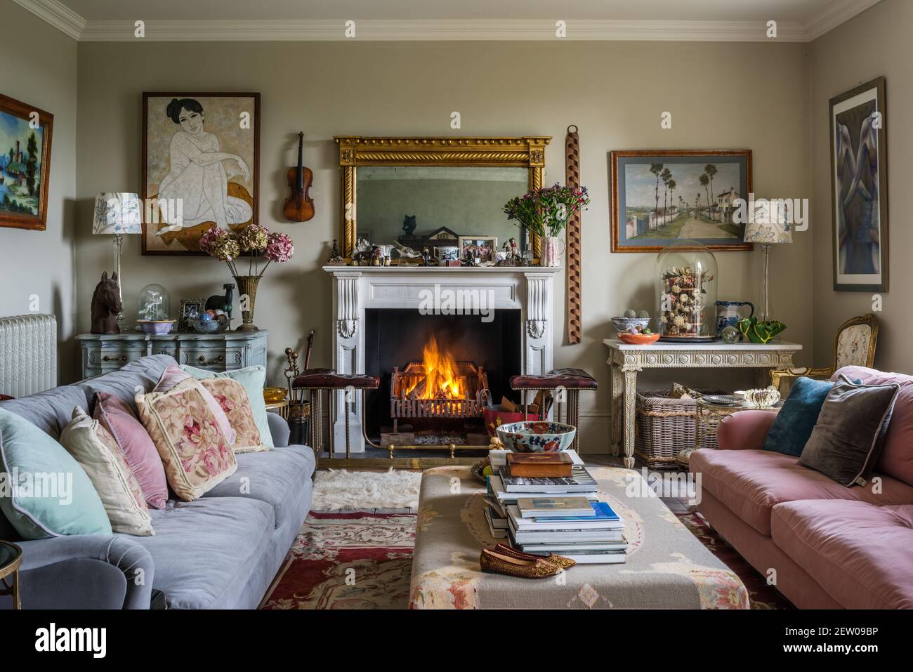 Collection of artwork with mismatched velvet sofas with lit fire in Dorset farmhouse Stock Photo