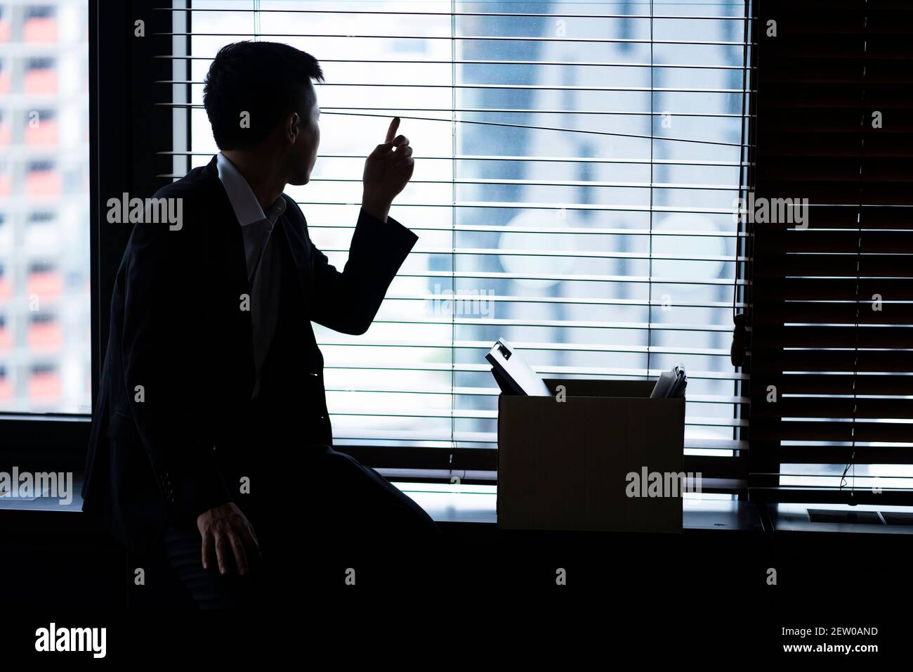 Fired businessman sitting with box of belongings by window Stock Photo
