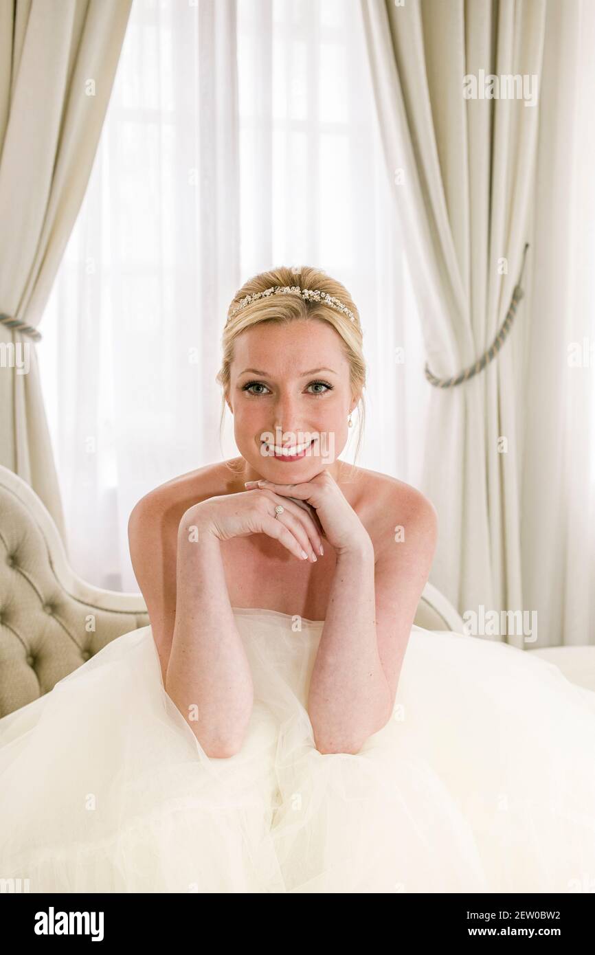 Bride sitting down on chaise lounge within bridal suit Stock Photo