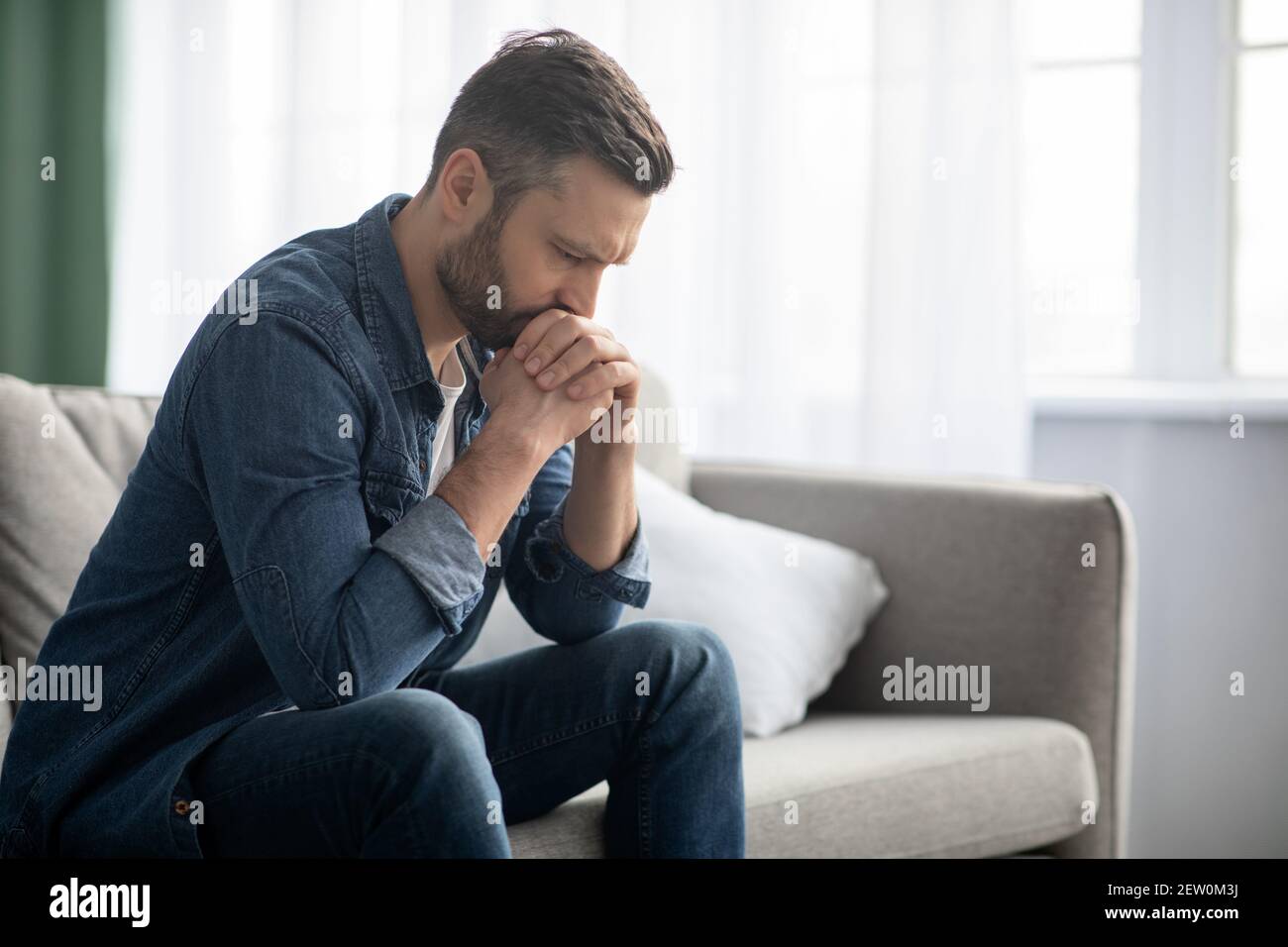 Sad man sitting on couch at home, side view Stock Photo - Alamy