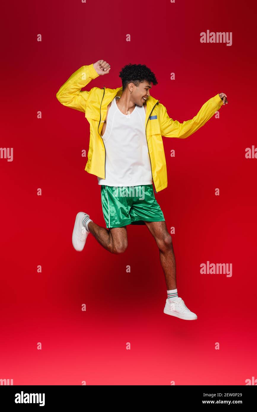 full length of cheerful african american man in yellow jacket jumping on red Stock Photo