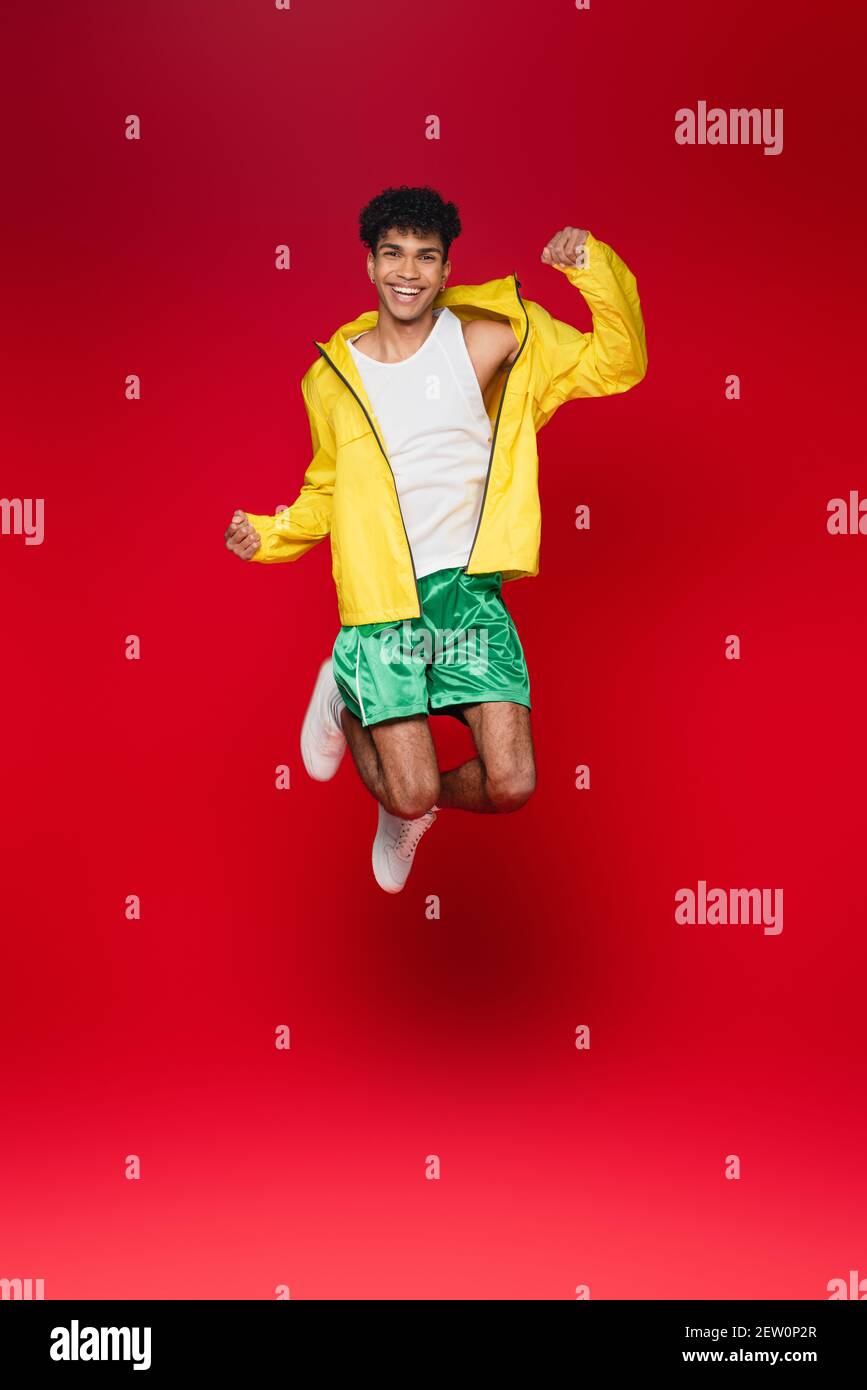 full length of smiling african american man in yellow jacket jumping on red Stock Photo