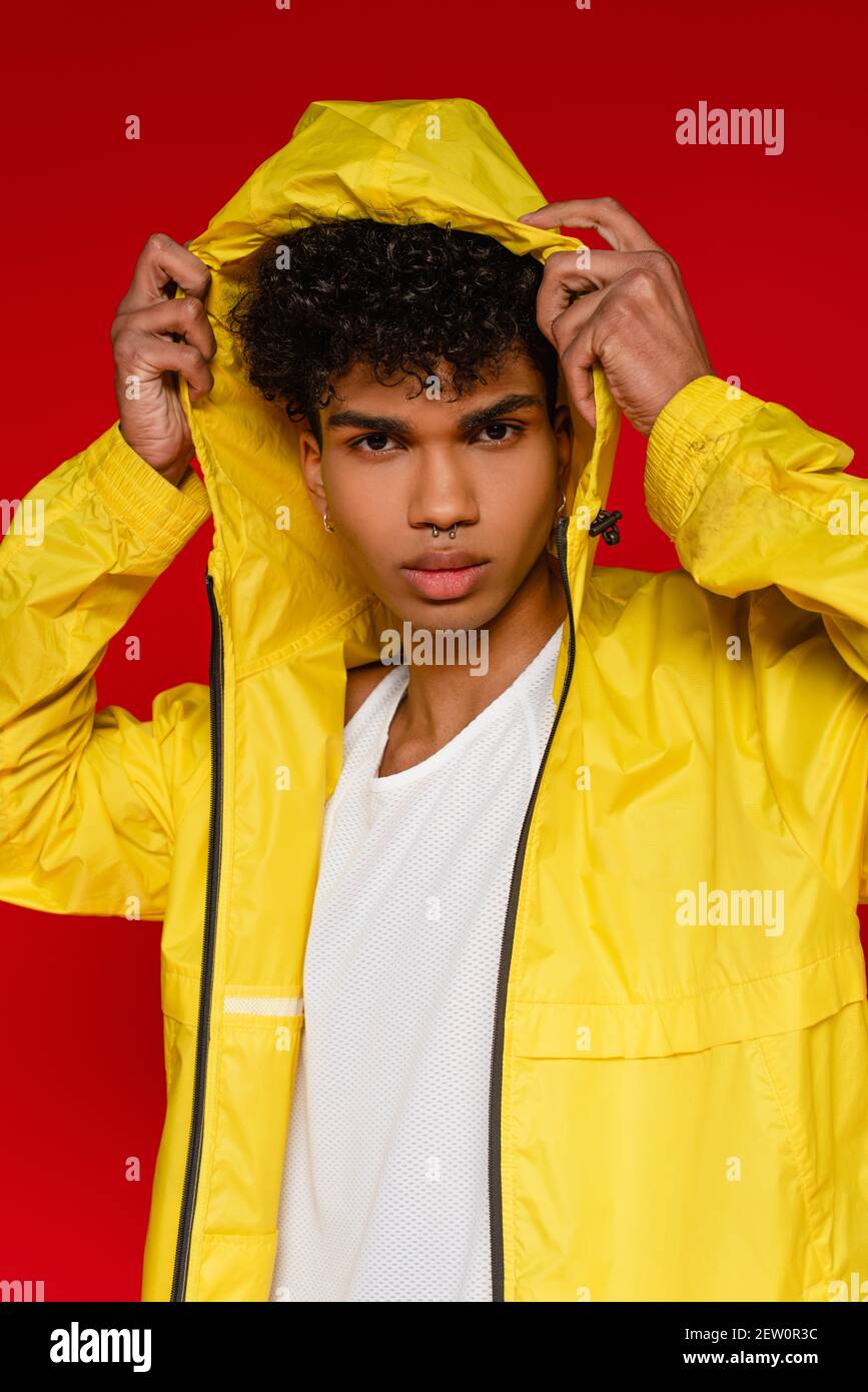 stylish african american man in yellow rain jacket adjusting hood isolated on red Stock Photo
