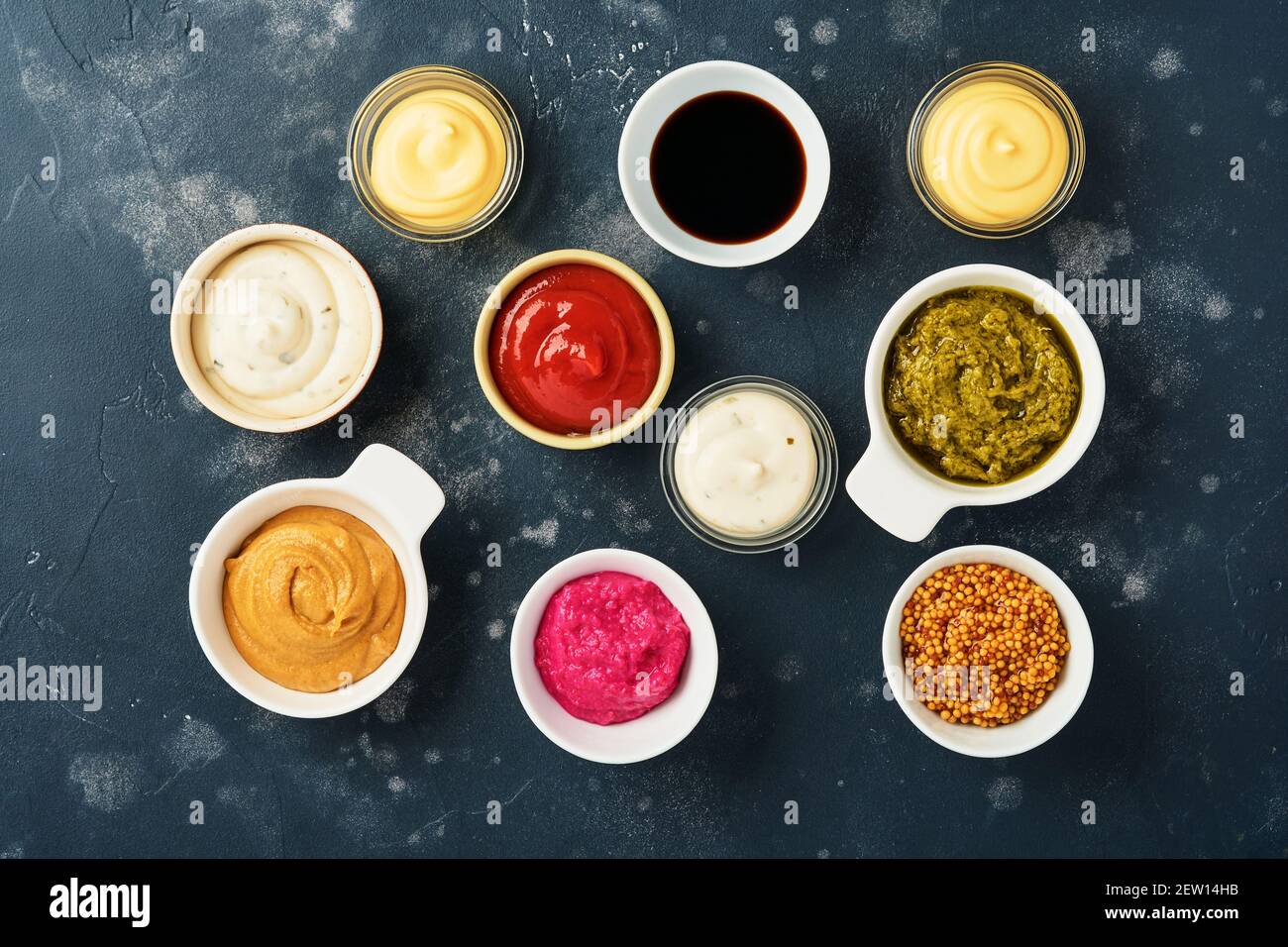 Set of sauces in bowls - ketchup, mayonnaise, mustard, soy sauce, bbq sauce, pesto, chimichurri, mustard grains on dark stone background. Top view cop Stock Photo