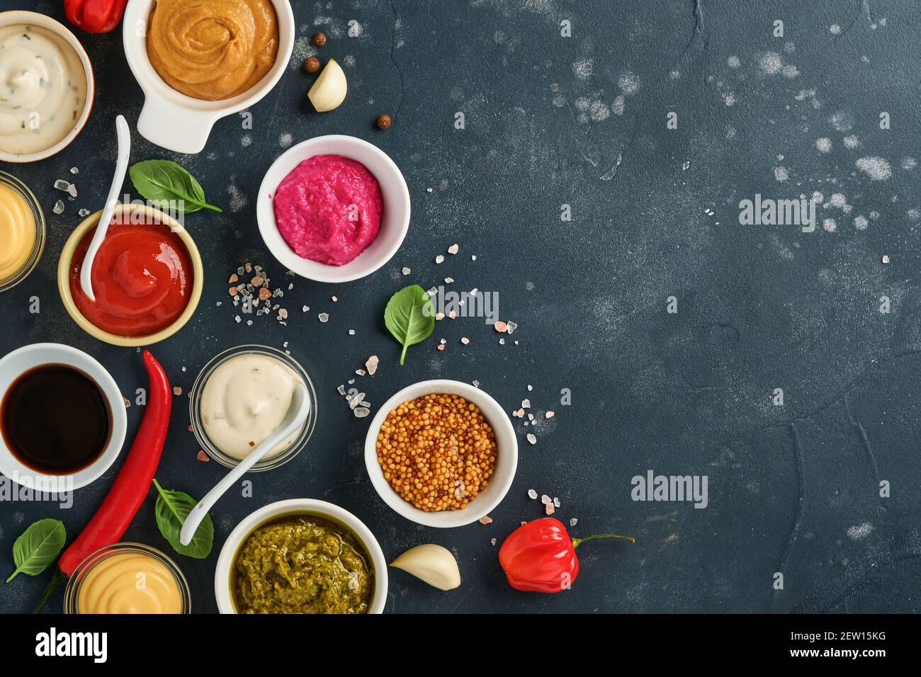 Set of sauces in bowls - ketchup, mayonnaise, mustard, soy sauce, bbq sauce, pesto, chimichurri, mustard grains on dark stone background. Top view cop Stock Photo