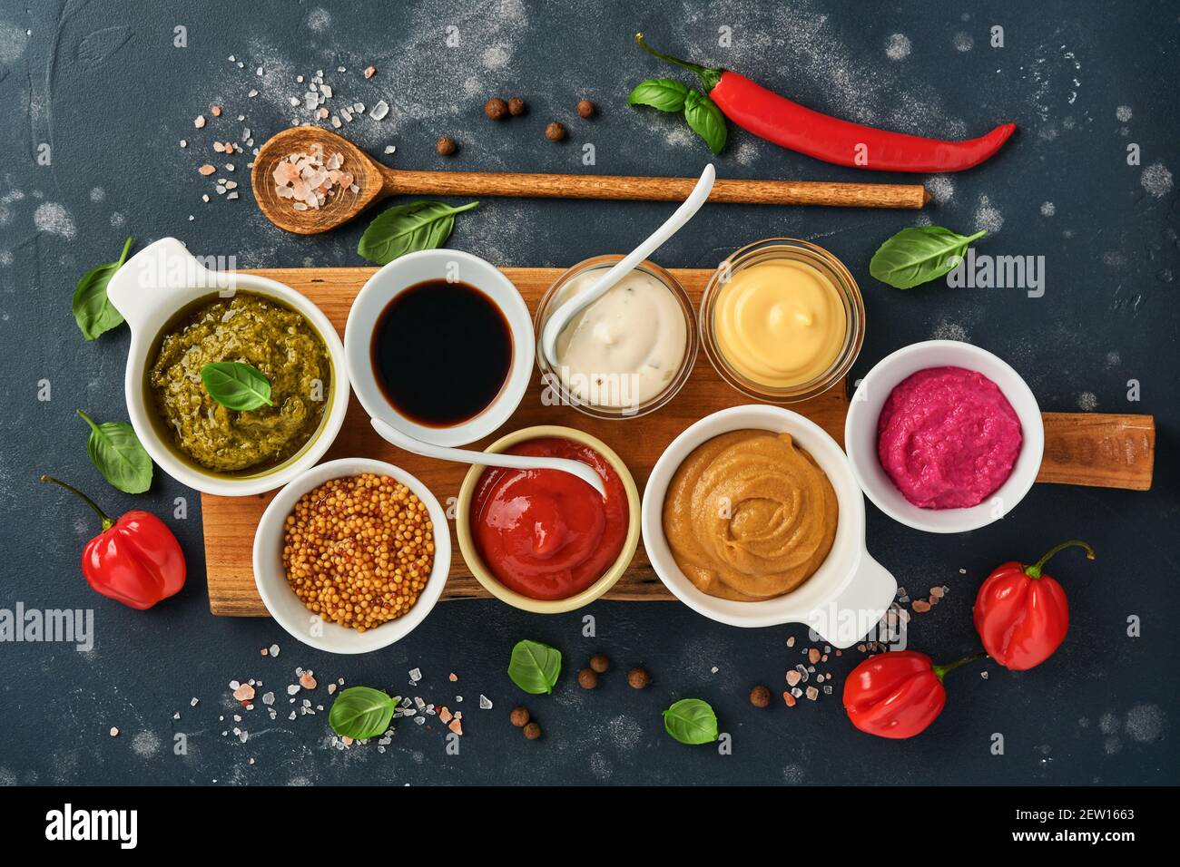 Set of sauces in bowls - ketchup, mayonnaise, mustard, soy sauce, bbq sauce, pesto, chimichurri, mustard grains on dark stone background. Top view cop Stock Photo