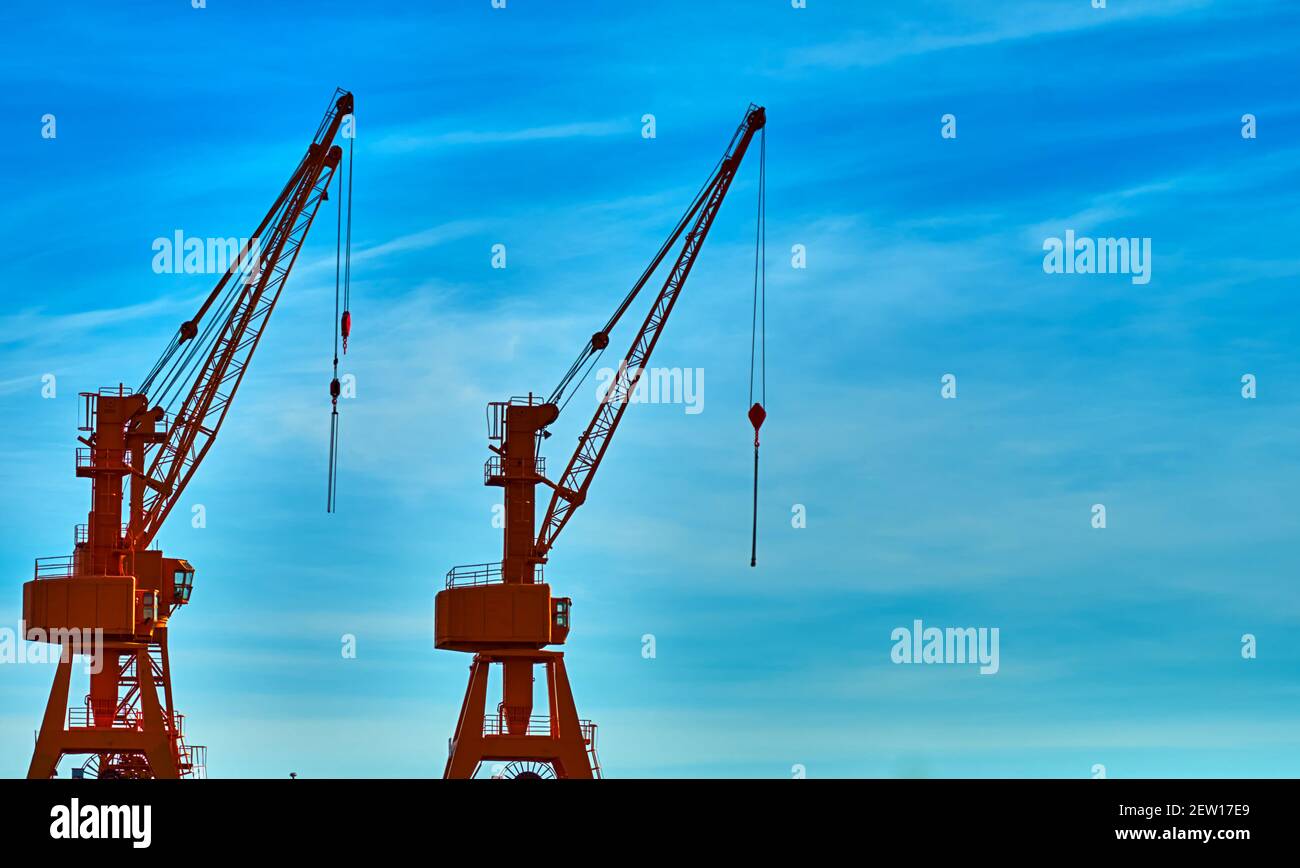 Cargo cranes on the harbor quay against a sky with hazy veil clouds Stock Photo