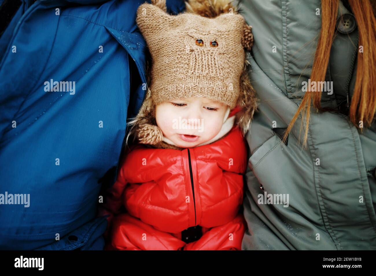 Concept of parental care, portrait of cute unhappy sad little girl in warm outfit sitting between her parents in wintertime Stock Photo