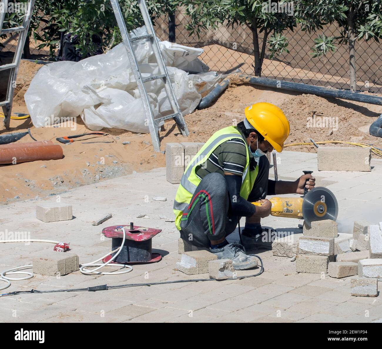 A working sitting using a angle grinder to grind cement bricks to the correct size Stock Photo