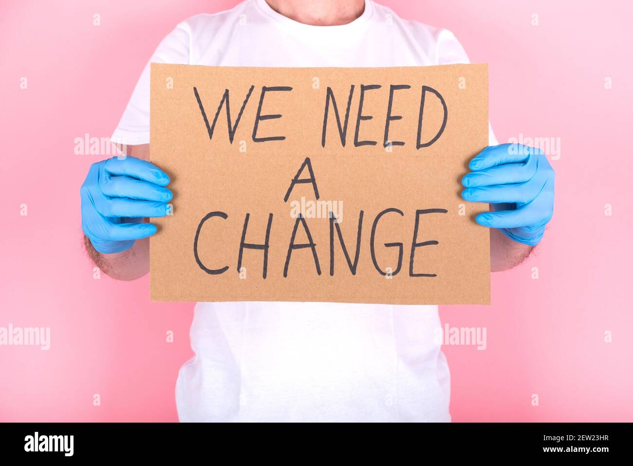 cardboard with the message WE NEED A CHANGE. Anonymous hands protected with gloves hold the protest poster Stock Photo