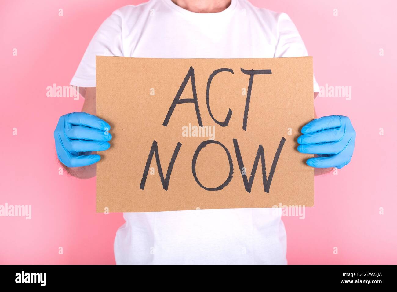 cardboard with ACT NOW message. Anonymous hands protected with gloves hold the protest poster Stock Photo