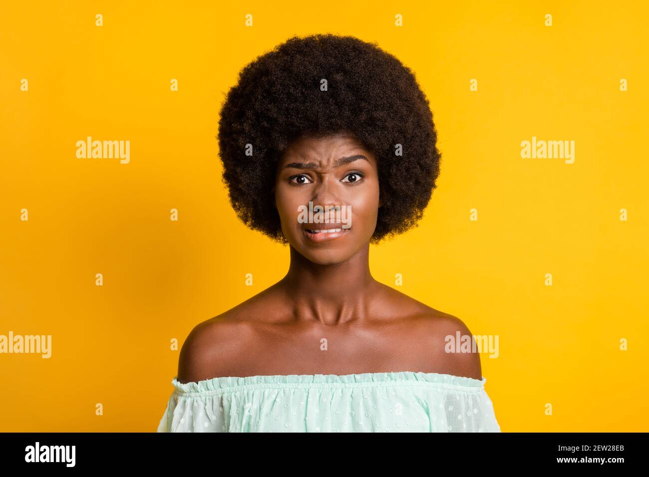 Photo portrait of confused girl biting lower lip isolated on vivid yellow colored background Stock Photo