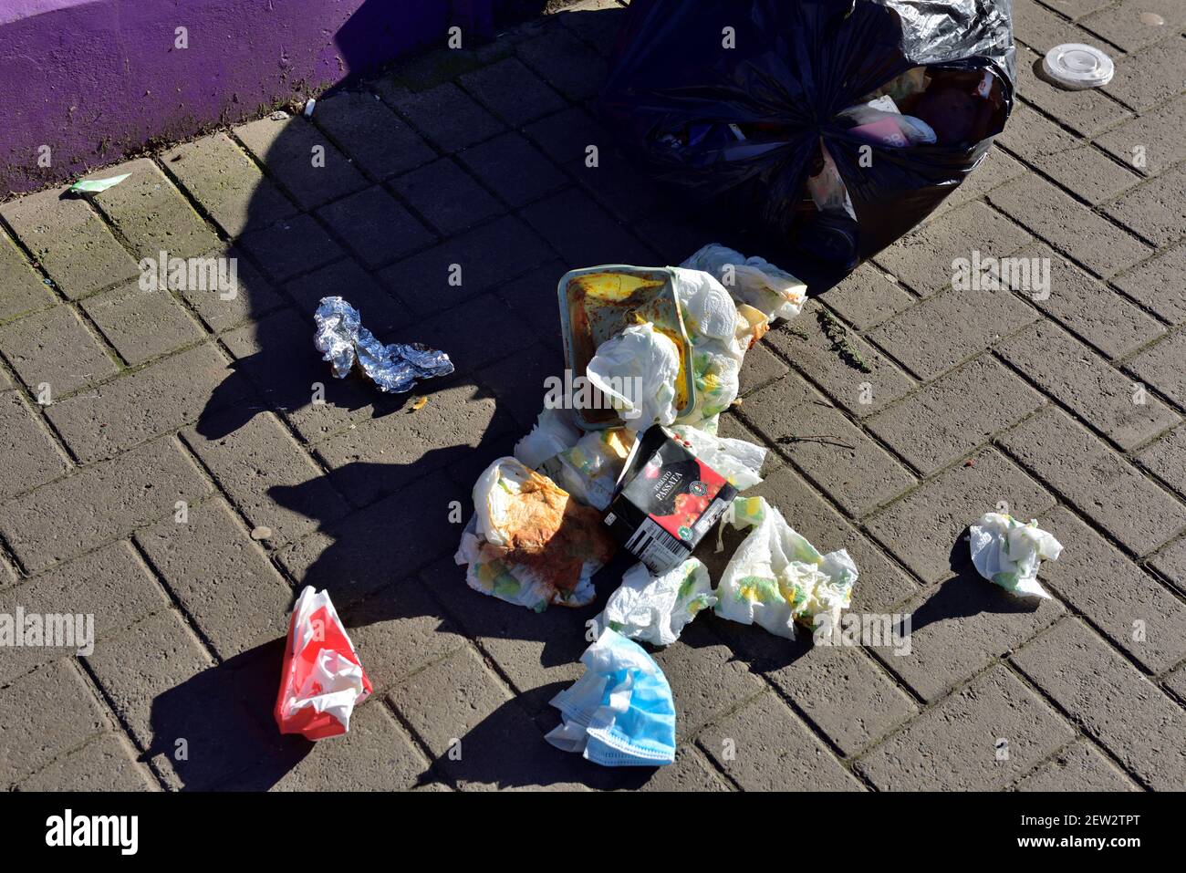 Rubbish strewn across pavement from broken open black plastic bin liner Stock Photo