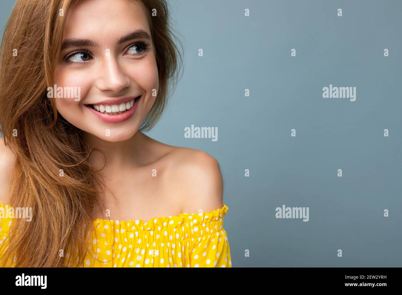 Closeup of young smiling charming dark blonde woman with sincere emotions isolated on background wall with copy space wearing stylish yellow dress Stock Photo