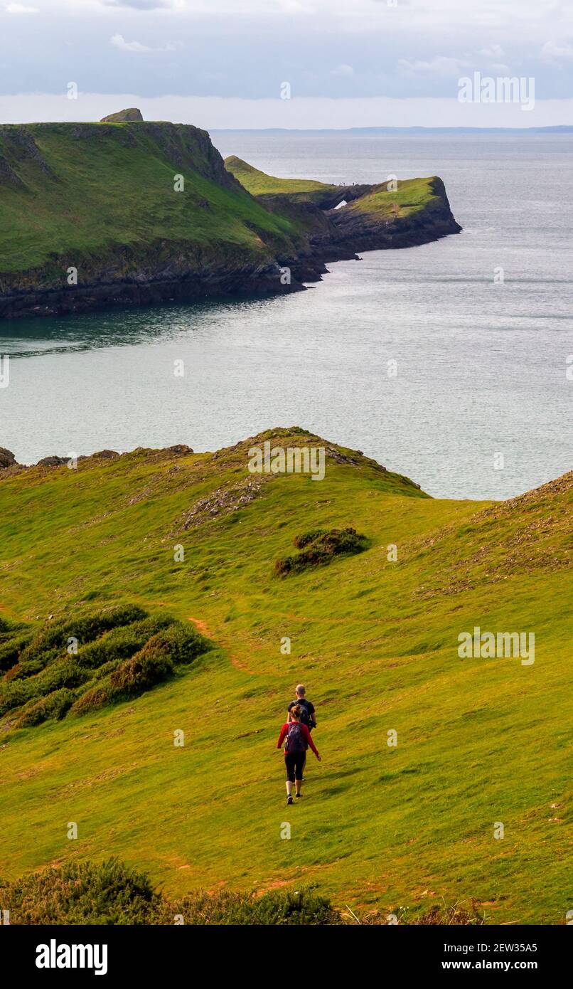 Couple walking towards Worms Head a carboniferous limestone headland on the western side of the Gower Peninsula near Swansea South Wales UK Stock Photo