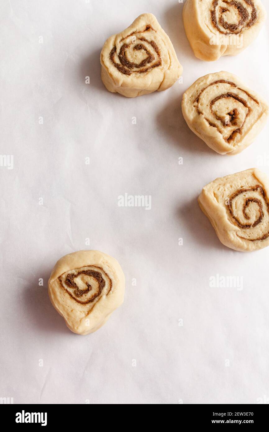 Slices of raw cinnamon rolls dough on a white baking paper background. Stock Photo